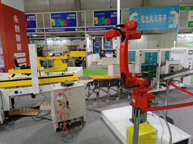 Eine Gruppe von Robotern auf einem Tisch umgeben von Maschinen und elektronischen Bauteilen in einer Fabrikumgebung mit ein paar Menschen im Hintergrund.