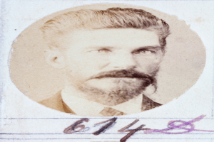 Ein altes Foto eines Mannes mit Bart und Schnurrbart, der direkt in die Kamera schaut und leicht geöffnete Lippen hat.