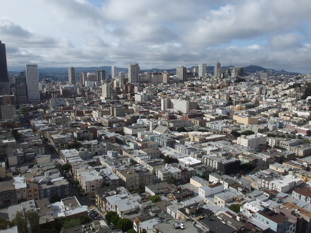 Eine dicht bebaute Stadtlandschaft mit zahlreichen Häusern, Gebäuden und hohen Türmen, mit minimaler Vegetation und einem sichtbaren Himmel im Hintergrund.