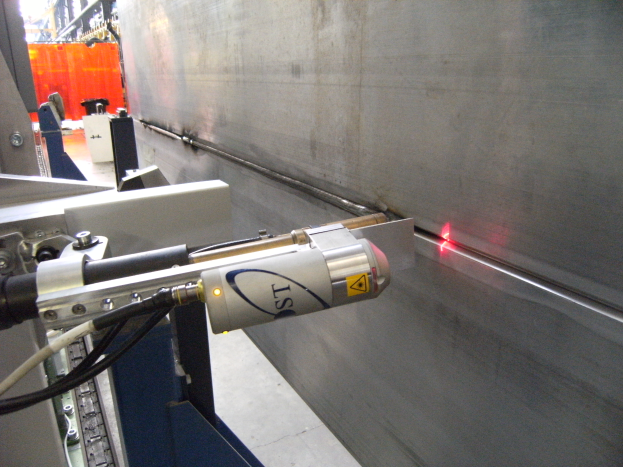 Eine Laserschneidemaschine in einer Fabrik strahlt helles Licht aus und erleuchtet die Umgebung mit einer Wand auf der rechten Seite und einigen Gegenständen im Hintergrund.