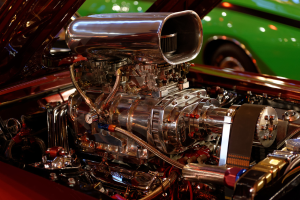 Eine Sammlung von Fahrzeugmotorteilen und anderen Komponenten mit einem im Hintergrund sichtbaren Auto.