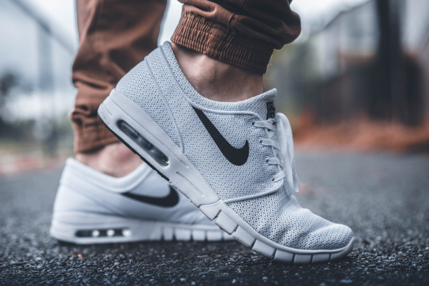 Nahaufnahme einer Person in schwarzen, weißen und grauen Nike SB Stefan Janoski Max-Schuhen vor einem unscharfen, nebligen Hintergrund.