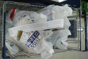 Ein Supermarktwagen voller plastikummantelter Artikel und eine Rechnung, mit einem grünen Korb in der oberen rechten Ecke.