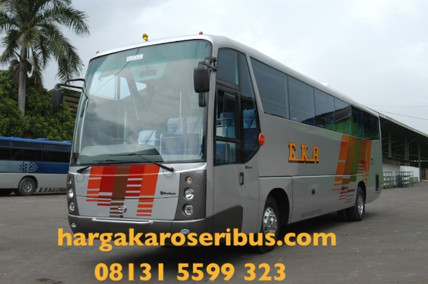 Ein grauer Bus in der Mitte, ein blauer Bus links, Bäume, ein Schuppen rechts, ein Himmel darüber und Kontaktinformationen unten.