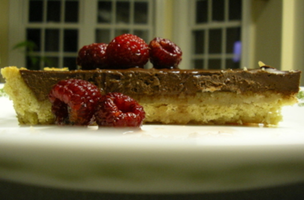 Eine Schokoladentorte mit Kirschen auf einem weißen Teller, vor einem weißen Glasfenster.