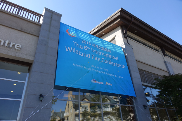 Außenansicht eines gläsernen Gebäudes, das die 6. Internationale Wildlandbrandkonferenz in Pjöngjang, Nordkorea, beherbergt, mit einem Banner und einem Baum.