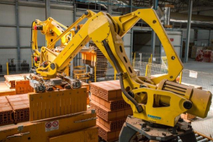 Ein großer Lagerraum voller numerous boxes, Kräne, ein Zaun, Pfosten und andere industrielle Ausrüstung, mit einer Wand im Hintergrund.