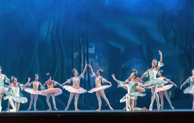 Eine Gruppe von Balletttänzern in farbenfrohen Kostümen performs *Der Nussknacker* auf der Bühne der Royal Opera House, bewegend sich in synchronisierter Anmut gegen einen blauen Hintergrund.