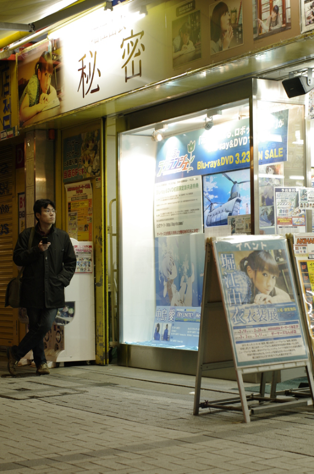 Ein Mann steht mit einem Mobiltelefon in der Hand, tragend eine Tasche, mit Schildern mit Text, Gesch√§ften, Lichtern und Papieren mit Text im Hintergrund.