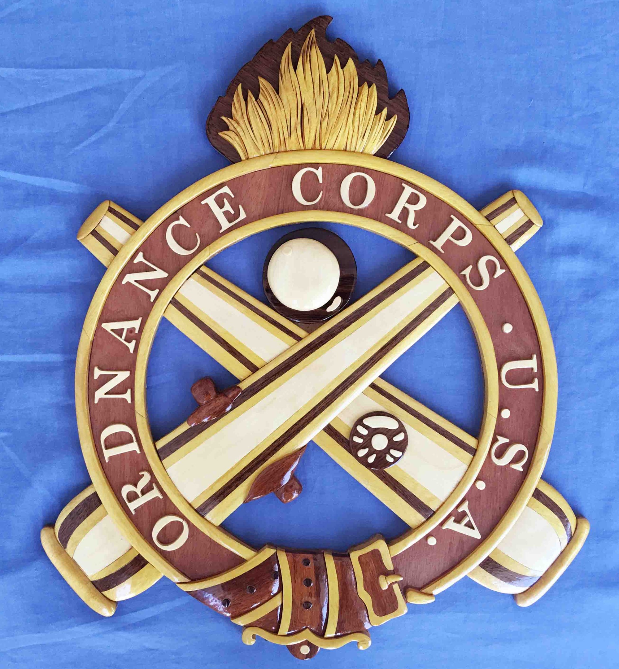 Ein hölzernes Schild mit den Worten "Ordnance Corps" in fetter schwarzer Schrift, mit einem navyblauen Hintergrund, einem weißen Stern und einem goldenen Rand, auf blauem Stoff montiert.