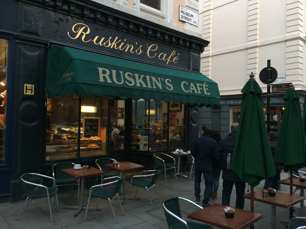 Eine Gruppe von Menschen steht vor einem Cafe mit der Aufschrift "Ruskin's Cafe".