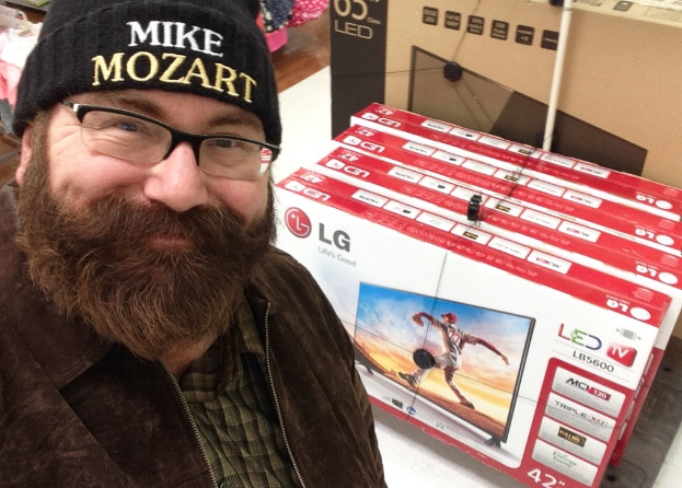 Eine Person, die vor Fernsehgeräten in Kartons und anderen Gegenständen lächelt.