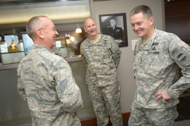 Drei uniformierte M├Ąnner stehen und l├Ącheln vor einer Wand mit einem Fotoраhmen, einem Glasfenster mit Laternen und Tischen und einer braunen T├╝r auf der rechten Seite.