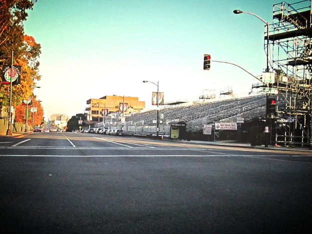 Eine Straße mit einem Verkehrszeichenmast und Equipment auf der rechten Seite, Warnschilder und mehrere Fahrzeuge vor zahlreichen Bäumen auf der linken Seite.