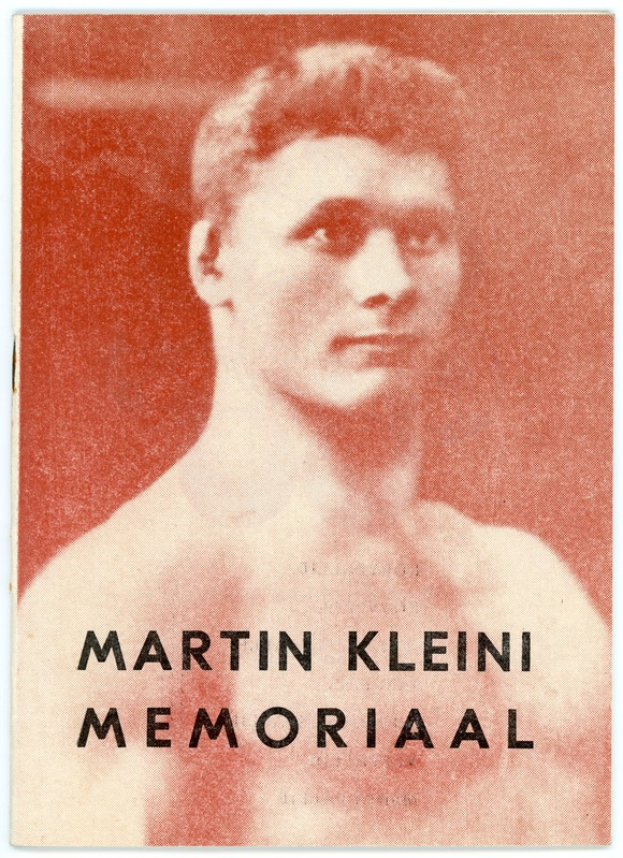 Ein Mann mit ernstem Gesichtsausdruck, der ein weißes Hemd und dunkle Hosen trägt, mit zurückgekämmtem Haar, der direkt in die Kamera schaut, mit dem Text "Martin Klein Memorial" unten.