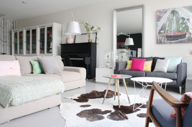 Ein Wohnzimmer mit zwei Sofas, zwei Tischen, einer Lampe, einem Kissen, einem Spiegel, einem Musikinstrument und einer Vitrine an der Wand.