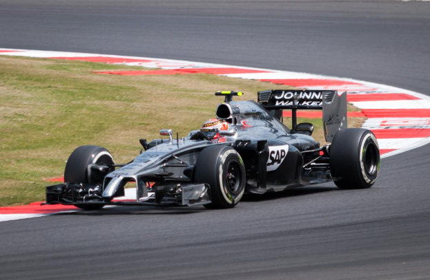 Ein Rennwagen fährt auf einer leeren Straße mit einer Grasfläche im Hintergrund.