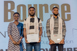 Drei Personen stehen nebeneinander auf einer Bühne und halten jeweils ein Zertifikat in der Hand, im Hintergrund ist ein Bildschirm mit der Aufschrift "Bounce Africa Awards 2019" zu sehen.