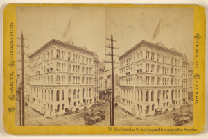 Ein altes Foto einer Stadtstraße mit Gebäuden, Strommasten und Karren, das Fenster an den Gebäuden und Text auf dem Bild zeigt.