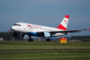 Ein Airbus A320-200 der Austrian Airlines startet vom Frankfurter Flughafen, mit einer Tafel im Vordergrund, Gras, Bäumen und Gebäuden im Hintergrund und einem klaren blauen Himmel.