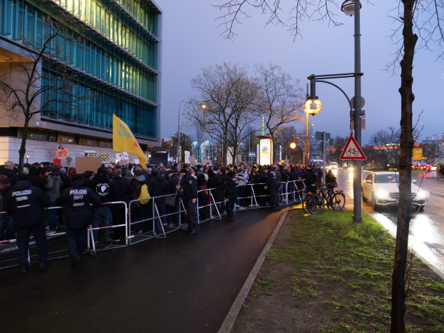 Große Gruppe von Menschen mit Schildern vor einem Gebäude mit Barrikaden, Fahrrädern und Schildern, was auf eine Protestaktion in Berlin hinweist.