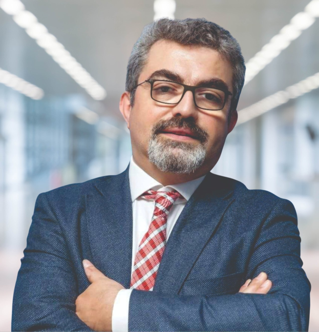 Ein Mann in Anzug und Krawatte mit verschränkten Armen, Brille tragend, vor einem unscharfen Hintergrund stehend, als neuer Marketingchef bezeichnet.