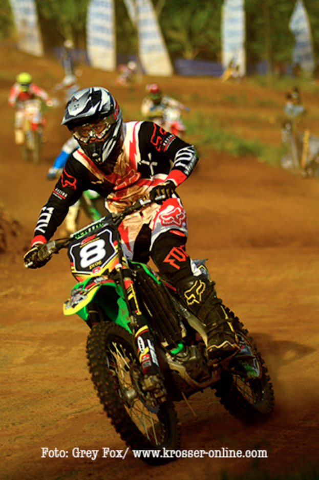 Mehrere Motorradfahrer mit Helmen rennen auf einer Strecke, mit Text am unteren Bildrand.