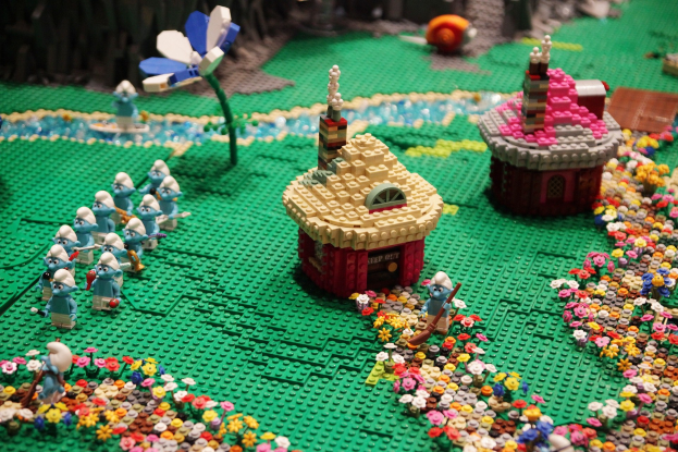 Ein Lego-Modell einer Kleinstadt mit Blumen, Spielzeugen, Häusern und Pflanzen vor einem unscharfen Hintergrund.