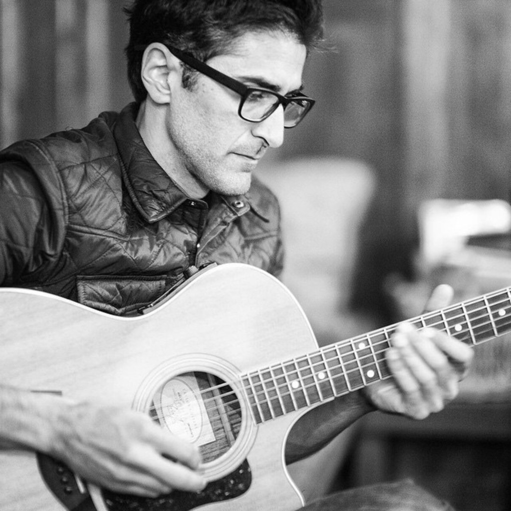 Ein Mann in einer Jacke spielt die Gitarre.