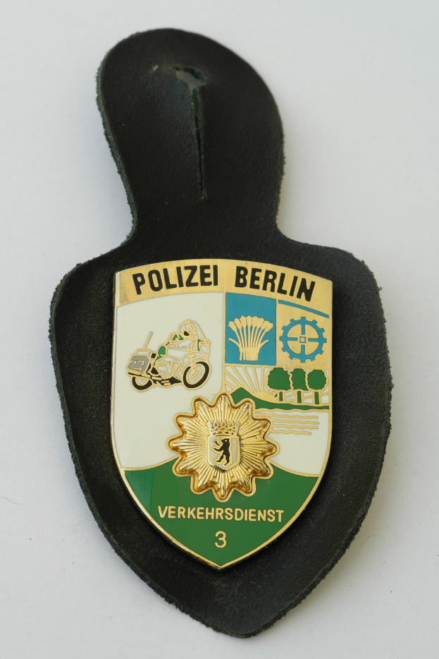 Ein schildförmiges Polize abadge mit 'Polizei Berlin' in schwarzer fettgeschriebener Schrift auf einem blauen Hintergrund mit einem weißen Stern und Rahmen, das auf einer Oberfläche ruht.