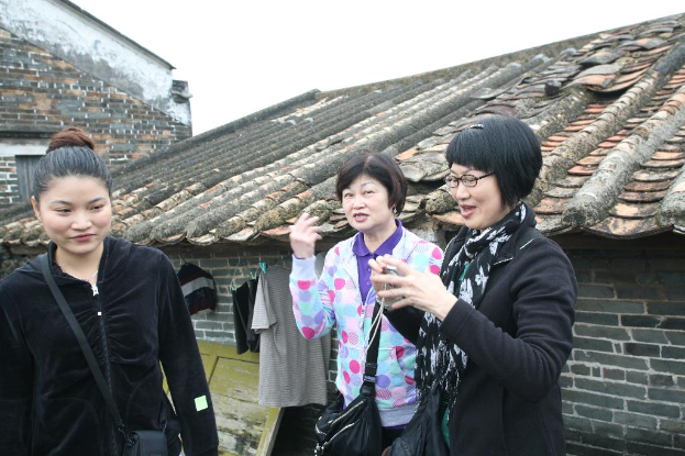 Drei Frauen, zwei davon lächeln und eine trägt eine Brille, mit Häusern und Himmel im Hintergrund.