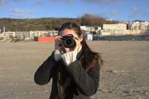 Eine Frau mit einer Kamera vor Gebäuden.