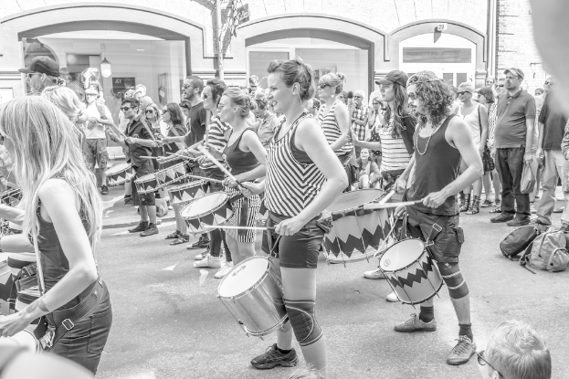 Eine Gruppe von Menschen, die musikalische Instrumente im Freien spielen, in der Nähe einer geschlossenen Glastür mit Licht im Hintergrund.