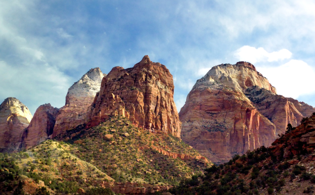 Zion National Park in Utah mit majestätischen Bergen, üppigen Bäumen, steinigem Gelände und einem Himmel voller weißer Wolken.