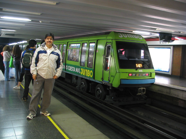 Ein Zug auf den Schienen mit Menschen auf der linken Seite und einem Dach oben im Bild.