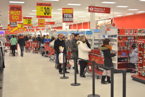 Ein volles Walmart-Geschäft mit Einkaufstüten tragenden Kunden und Einkaufswagen, umgeben von Warenauslagen, Schildern und Deckenleuchten.