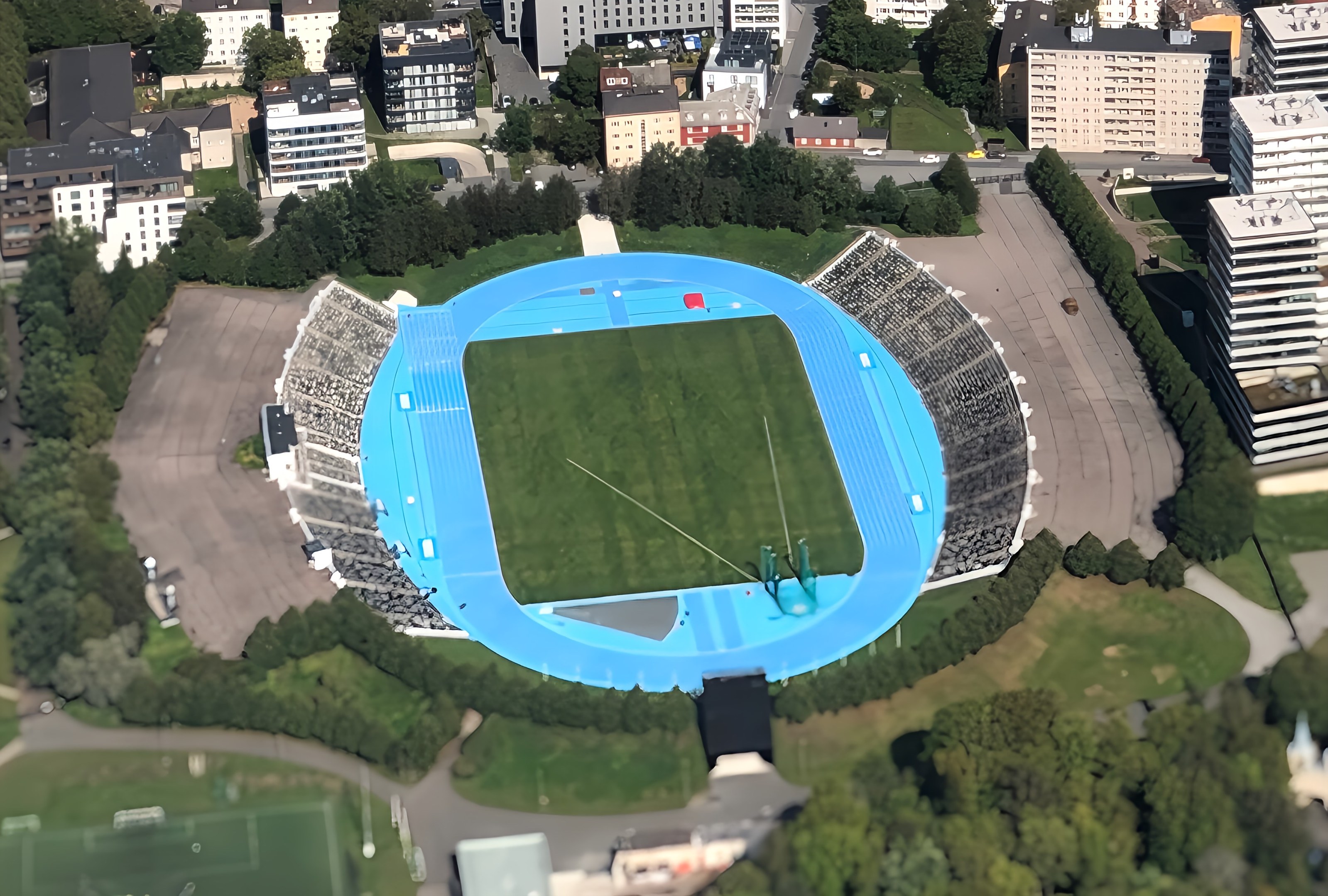 Luftaufnahme des Olympiastadions in München, Deutschland, umgeben von Stadtgebäuden, Bäumen, Straßen, Fahrzeugen und Gras.
