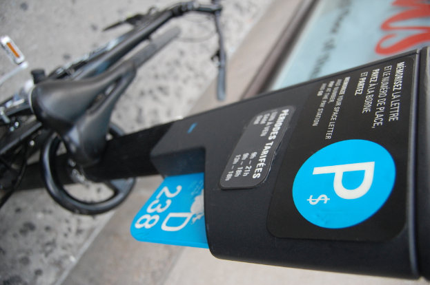 Ein Fahrrad steht auf dem Boden neben einem Parkautomaten mit einem gepflasterten Gehweg im Vordergrund.