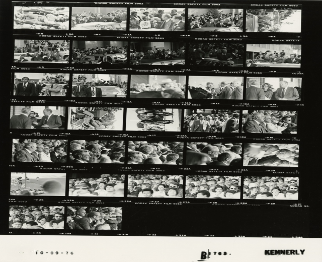 Schwarzes und weißes Foto einer vielseitigen Menge, die lachend auf einen Fernseher schaut.