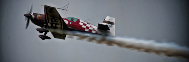 Ein rotes Flugzeug mit Entwürfen darauf, das durch die Luft fliegt und eine Rauchspur hinterlässt.