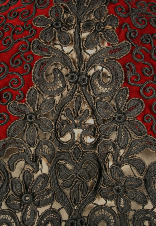 Nahaufnahme eines roten Kleids mit schwarzer Spitzenüberlagerung, das detaillierte Spitzenmuster auf dem leuchtenden roten Stoff zeigt.