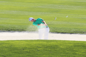 Ein Mann spielt Golf auf einem Platz mit grünem Gras, einem Wasserhindernis in der Mitte und mehr grünem Gras im Hintergrund.