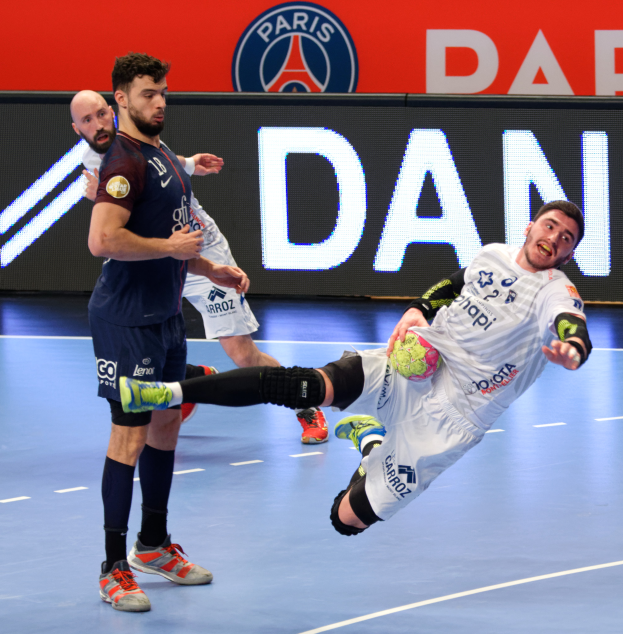 Eine Gruppe von Männern, die Handball auf einem Platz spielen, einer hält einen Ball, im Hintergrund ein Paris-Saint-Germain-Futsal-Team-Schild.