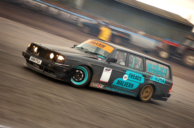 Ein Auto fährt eine Rennstrecke entlang, umgeben von anderen Fahrzeugen, mit einer Person darin, der Hintergrund durch die Bewegung unscharf.