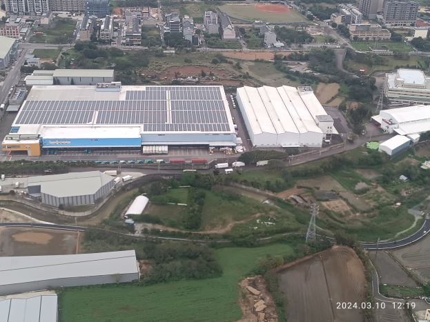 Eine Luftaufnahme eines großen Industriegebiets mit Gebäuden, Bäumen, Gras, Straßen, Fahrzeugen, Masten und einem Wasserzeichen, das es sich um die erste Solarstromanlage in Singapur handelt.