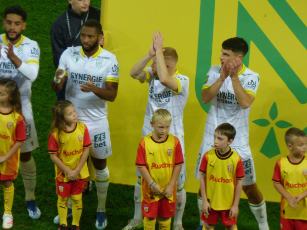 Eine Gruppe von Fußballspielern in Uniformen klatscht in Feierlaune auf einem Feld mit einem "Ligue 1"-Schild im Hintergrund.