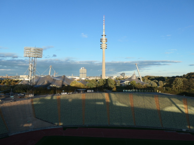 Olympiastadion in Berlin, Deutschland mit dem Fernsehturm im Hintergrund, umgeben von Bäumen, Gebäuden und Lichtern unter einem bewölktem Himmel.