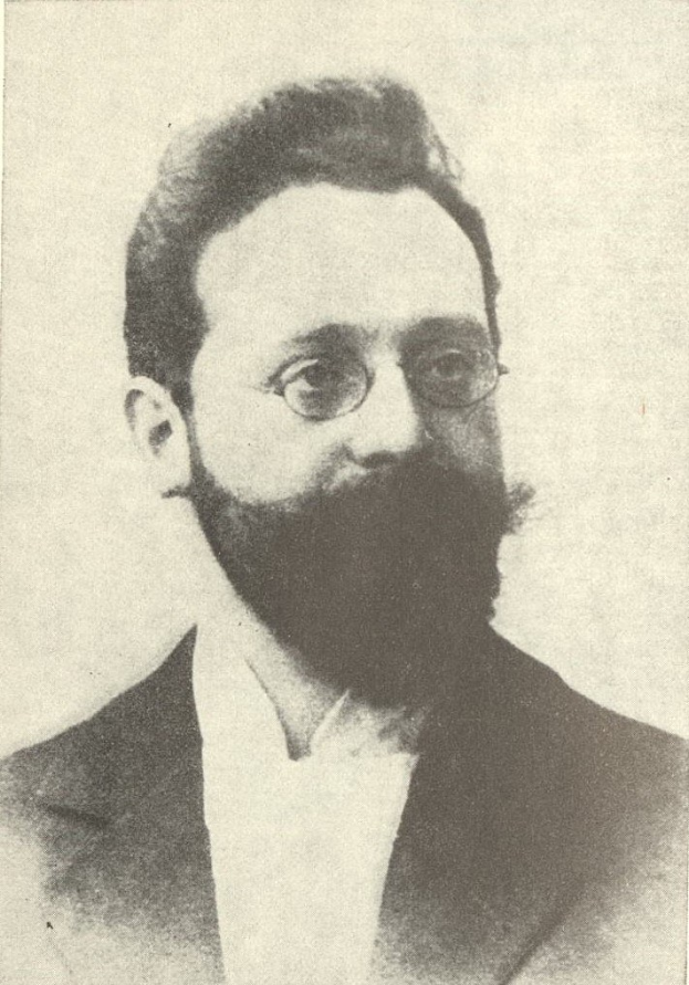 Schwarzes und weißes Porträt eines bärtigen Mannes in Anzug und Krawatte mit Brille, der ernsthaft in die Ferne schaut.