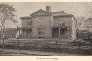 Ein Zaun mit Pfosten, Bäumen und Gebäuden im Hintergrund.