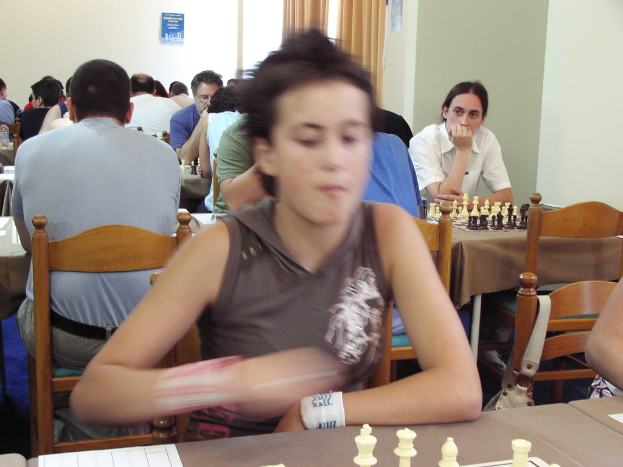 Ein Raum mit Menschen an Tischen, die Schach spielen, mit einer Vorhangwand und einem Foto in der Ecke.